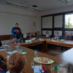 Grupa seniorów i seniorek uczestniczy w warsztatach w sali konferencyjnej.