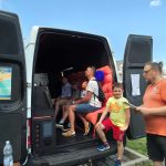 Na fotografii widać GRAtoWÓZ Fundacji GraTy, w którym grupa ludzi - zarówno dzieci, jak i dorośli - siedzi z uśmiechami na twarzach i gra na konsolach. Atmosfera jest pełna radości i entuzjazmu, pokazując, że dobra zabawa nie zna granic wiekowych. Fundacja GraTy promuje wspólne spędzanie czasu i integrację poprzez gry, także komputerowe, co doskonale widać na tym ujęciu.