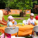 Rodzina bawi się przy planszówce na wydarzeniu organizowanym przez Fundację GraTy. Sprawiają wrażenie bardzo zgranego zespołu, a uśmiechy na ich twarzach mówią same za siebie.