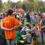 Wolontariusze prowadzą warsztaty z gier planszowych na świeżym powietrzu podczas festiwalu gier. W tle liczni uczestnicy eventu.