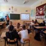 Uczniowie uczestniczą w prelekcji prowadzonej przez osobę z Fundacji GraTy, siedząc w klasie i słuchając prezentacji wyświetlanej na ekranie.