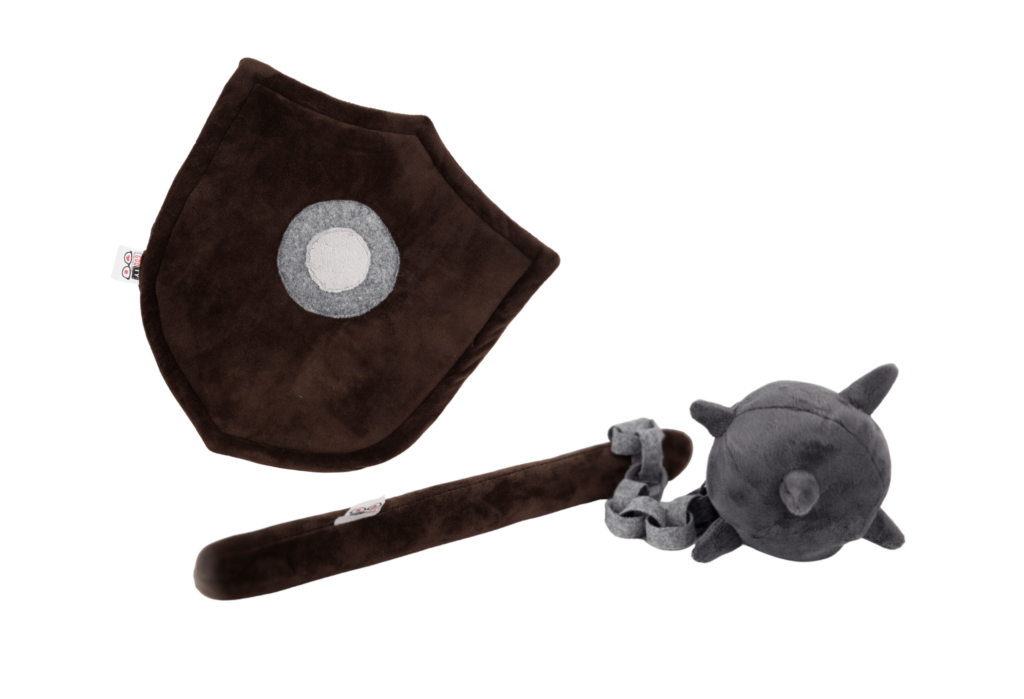Pluszowy zestaw do zabawy: ciemnobrązowa tarcza z jasnoszarym okręgiem pośrodku oraz ciemnoszara maczuga z kolcami, połączona sznurkiem z brązową rękojeścią, leżące na białym tle.
