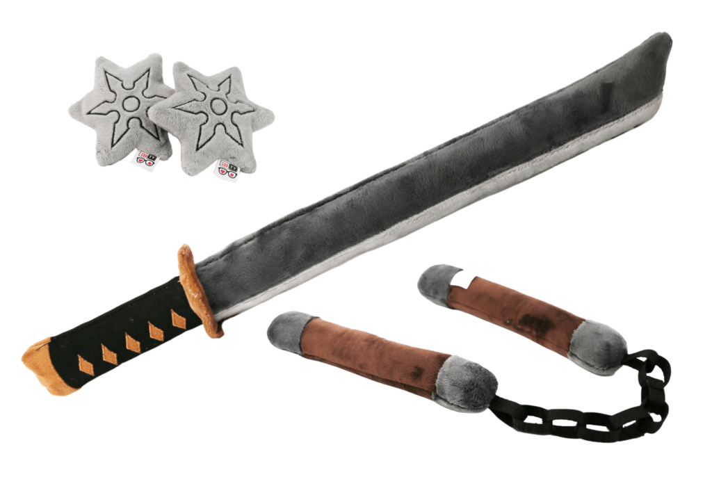 Pluszowy zestaw ninja: ciemnoszary miecz z jasnoszarą klingą i czarną rękojeścią, dwie jasnoszare gwiazdki ninja oraz brązowo-szare nunchaku z czarnym łańcuchem, leżące na białym tle.