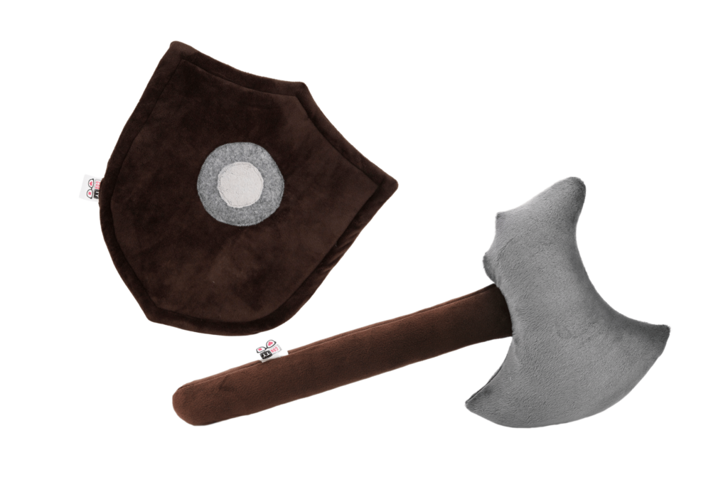 Pluszowa siekiera bądź topór jednosieczny o szarym ostrzu osadzonym na brązowym sztylu z miękkiego materiału. Obok pluszowa trójkątna tarcza z szarym kółkiem w jej środku,