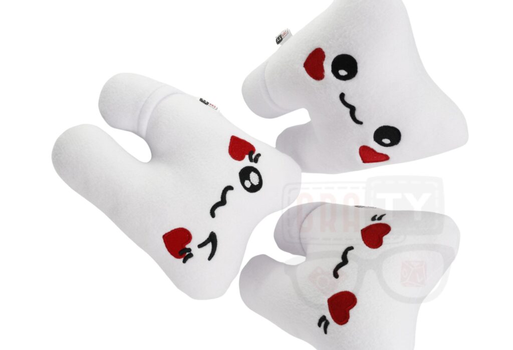 Trzy pluszowe zęby z haftowanymi czerwonymi sercami zamiast oczu i czarnymi uśmiechami, leżące na białym tle.