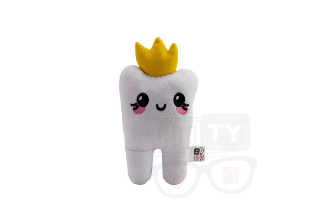 Pluszowy ząb z koroną, leżący na białym tle.