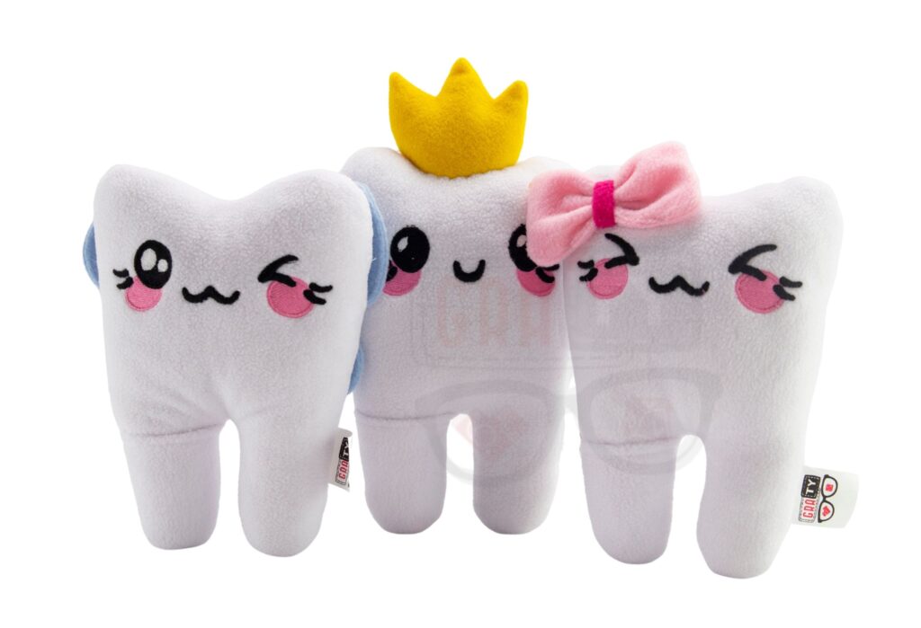 Trzy pluszowe zęby z akcesoriami: korona i kokarda, ułożone na białym tle.