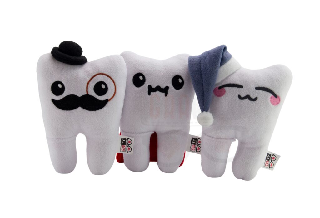 Trzy pluszowe zęby z różnymi akcesoriami: kapelusz i monokl, czapka do spania, ułożone na białym tle.