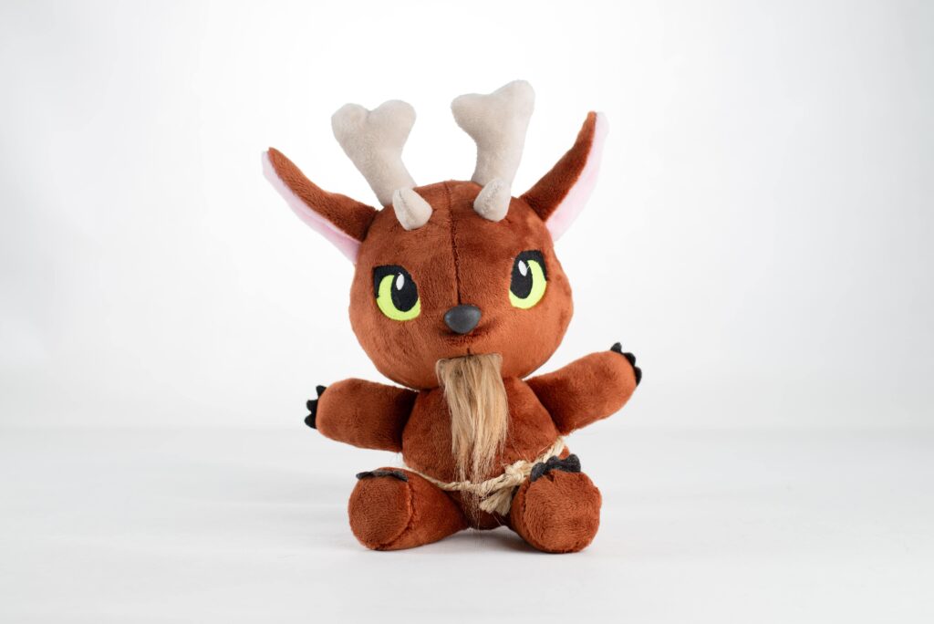 Pluszowy Bies – maskotka w brązowym kolorze z zielonymi oczami, spiczastymi uszami, kościanymi rogami i długą brodą, związana sznurem wokół pasa.